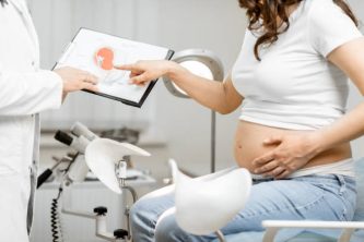 Doctor with pregnant woman during a medical consultation in gynecological office, showing some medical schemes for understanding, cropped view without faces